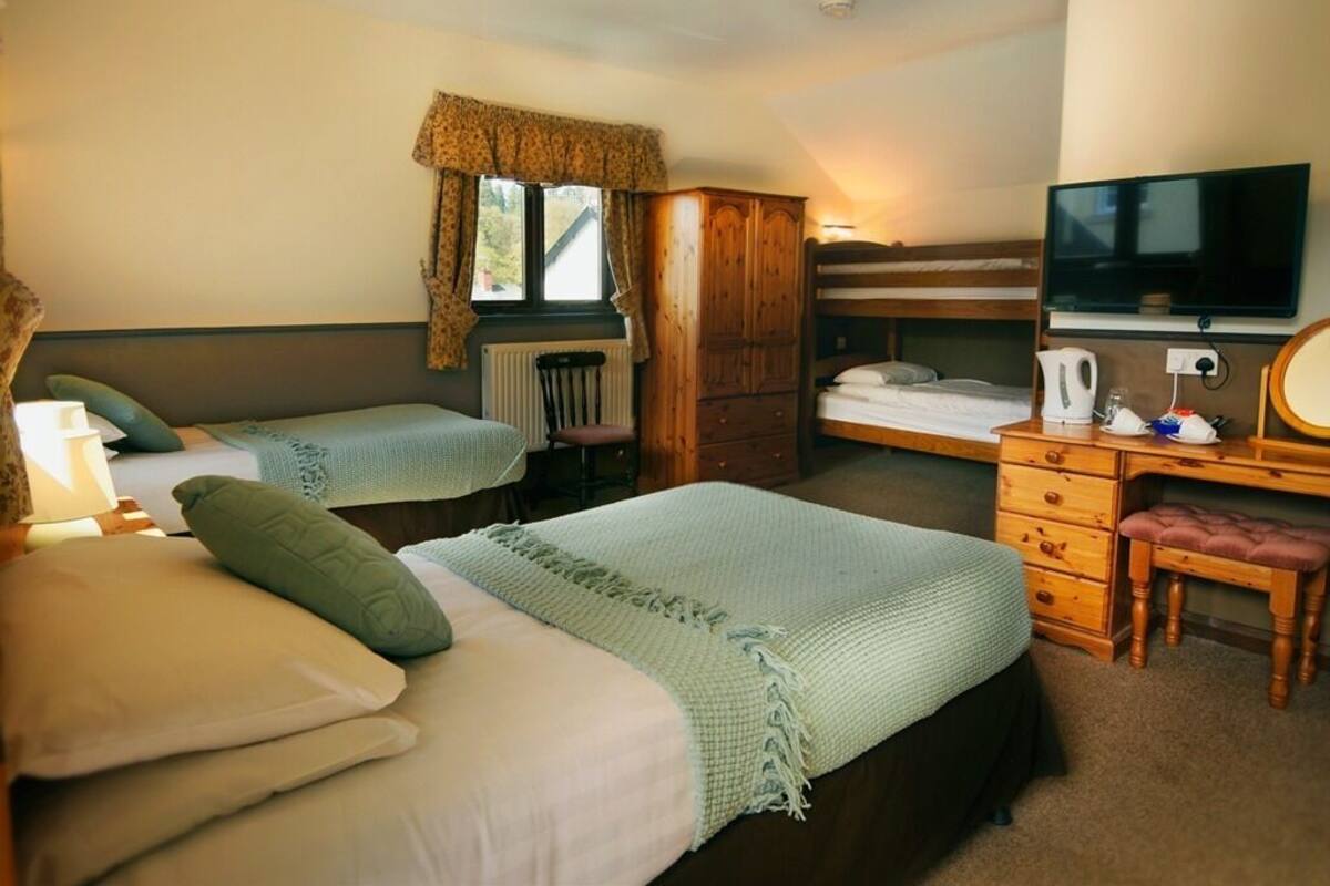 A bedroom with two beds, a wooden wardrobe, a desk with a chair, a television, and a window with curtains.
