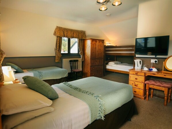 A bedroom with two beds, a wooden wardrobe, a desk with a chair, a television, and a window with curtains.
