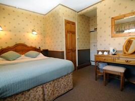 Un dormitorio con una cama, un aparador de madera, un espejo y una puerta que da a otra habitación.
