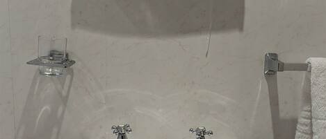 A bathroom with a white sink, two faucets, a mirror above the sink, and a shelf with toiletries.