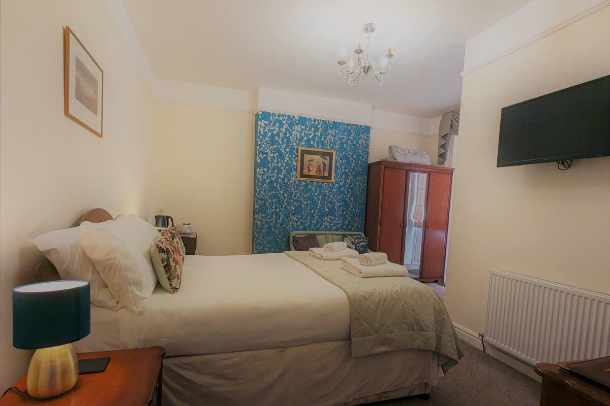 A hotel room with a bed, a nightstand, a lamp, a wardrobe, and a television on the wall.
