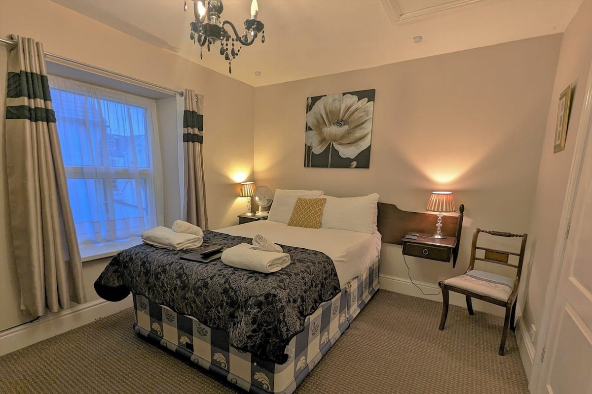 A hotel room with a large bed, a bedside table with a lamp, a chair, and a painting on the wall.