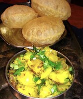 A plate of food with two types of items: a bowl of yellow curry with green herbs and a plate of round, golden-brown items.