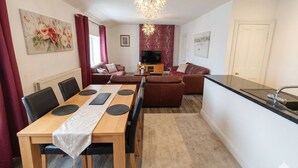 A modern kitchen with a dining area, a sofa set, and a TV. - The Senarth (Llandudno)