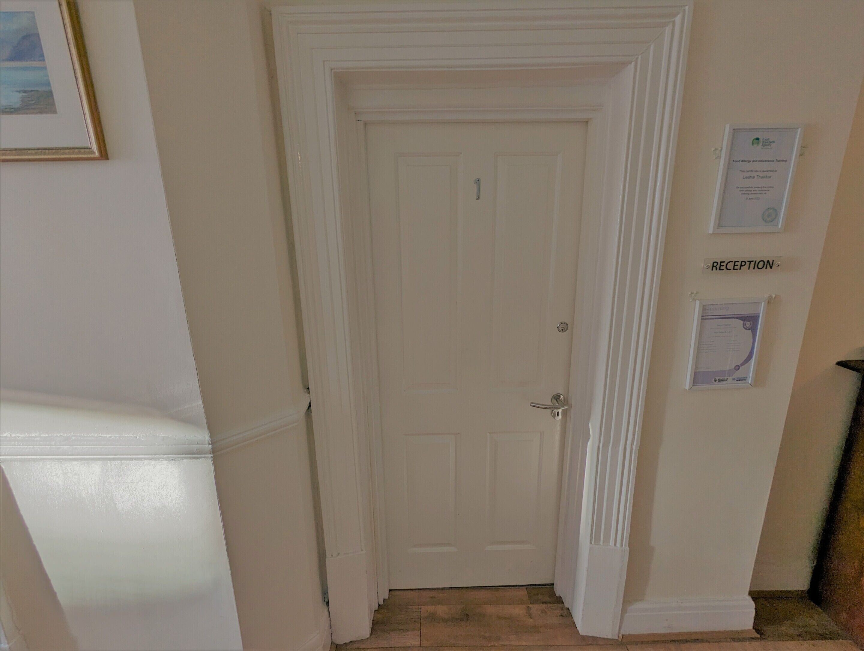 A reception area with a closed door, a framed certificate on the wall, and a sign indicating the reception location.