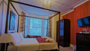 A four-poster bed with a red throw blanket, a television on the wall, and a large window with curtains. - The Senarth (Llandudno)