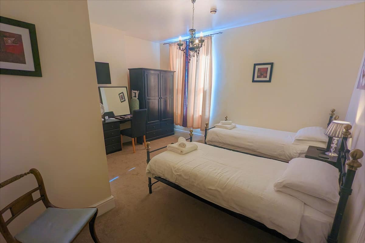 A bedroom with two beds, a desk, a chair, and a wardrobe.
