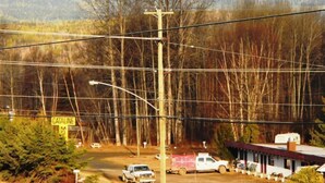 A road with a white pickup truck and a white van parked by the roadside. There is a building with a red roof in the background. - Cataline Motel & RV Park (South Hazelton)
