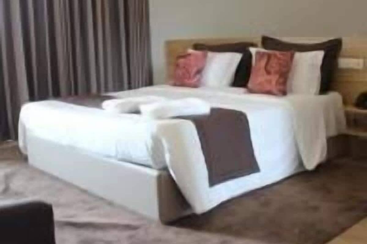 A hotel room with a large bed, a wooden headboard, a nightstand, and a window with curtains.