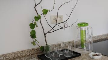 A kitchen counter with a branch, a green water dispenser, and four glasses.