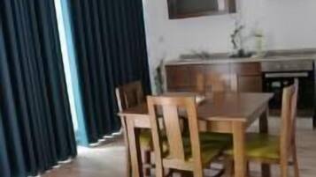 Un comedor con una mesa y sillas de madera, una cocina con microondas y estufa, y cortinas oscuras.