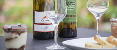 A table with a bottle of Louis Fran wine, a glass, a jar of food, and a plate with bread.