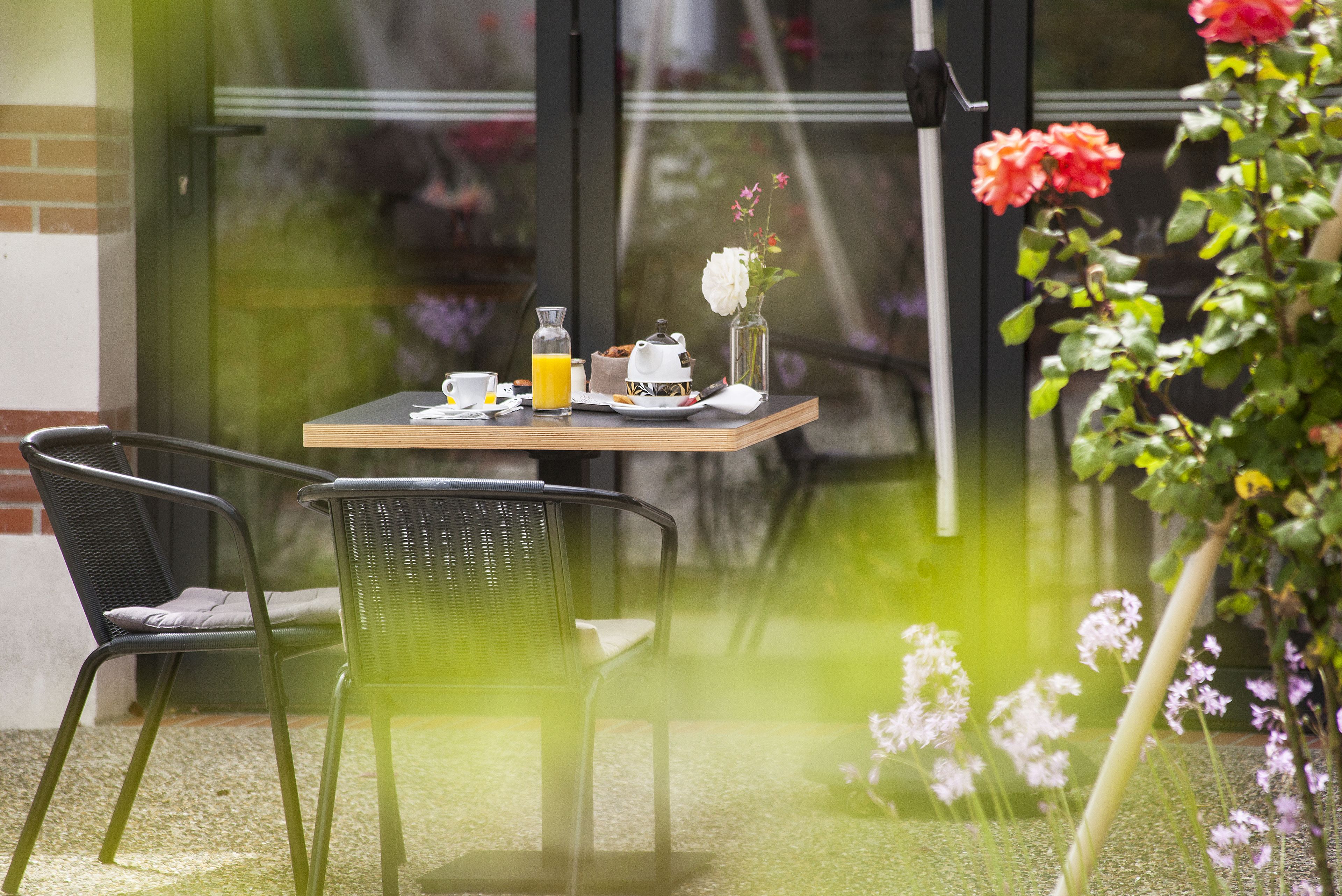 Una mesa dispuesta con alimentos para el desayuno, una silla y un jarrón de flores.