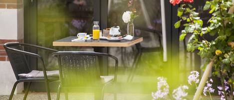 Una mesa dispuesta con alimentos para el desayuno, una silla y un jarrón de flores.