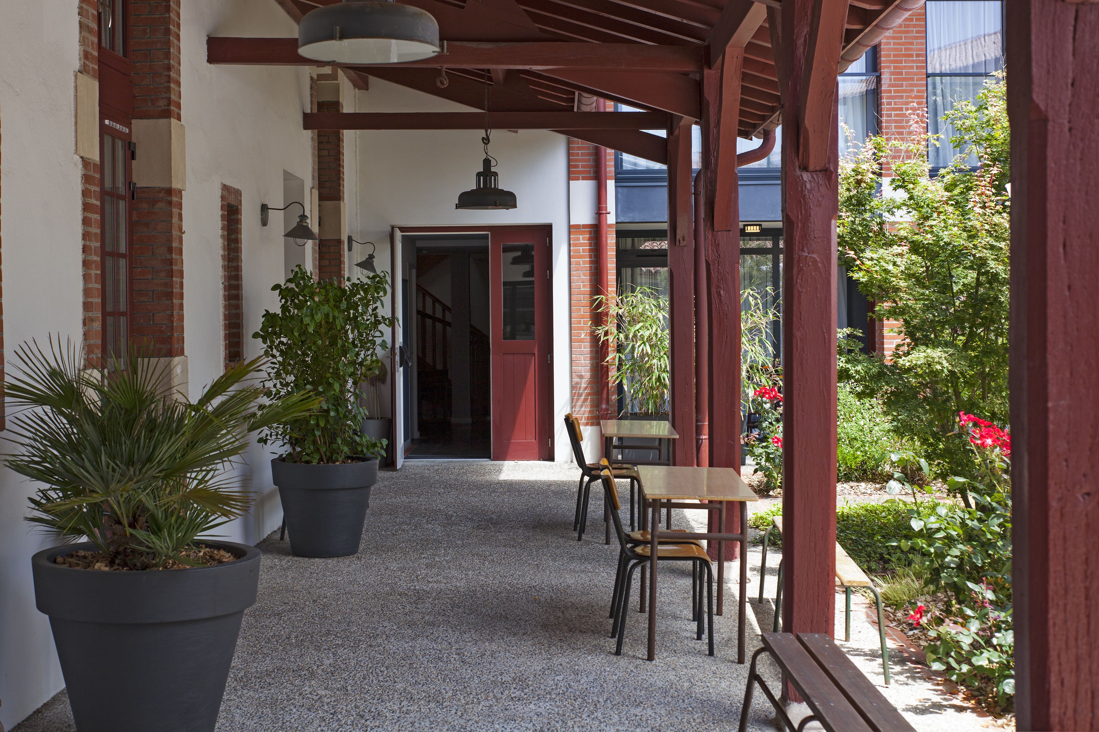 Ein überdachter Patio-Bereich mit Kiesboden, Topfpflanzen, einer Holzbank und einem Tisch mit Stühlen.