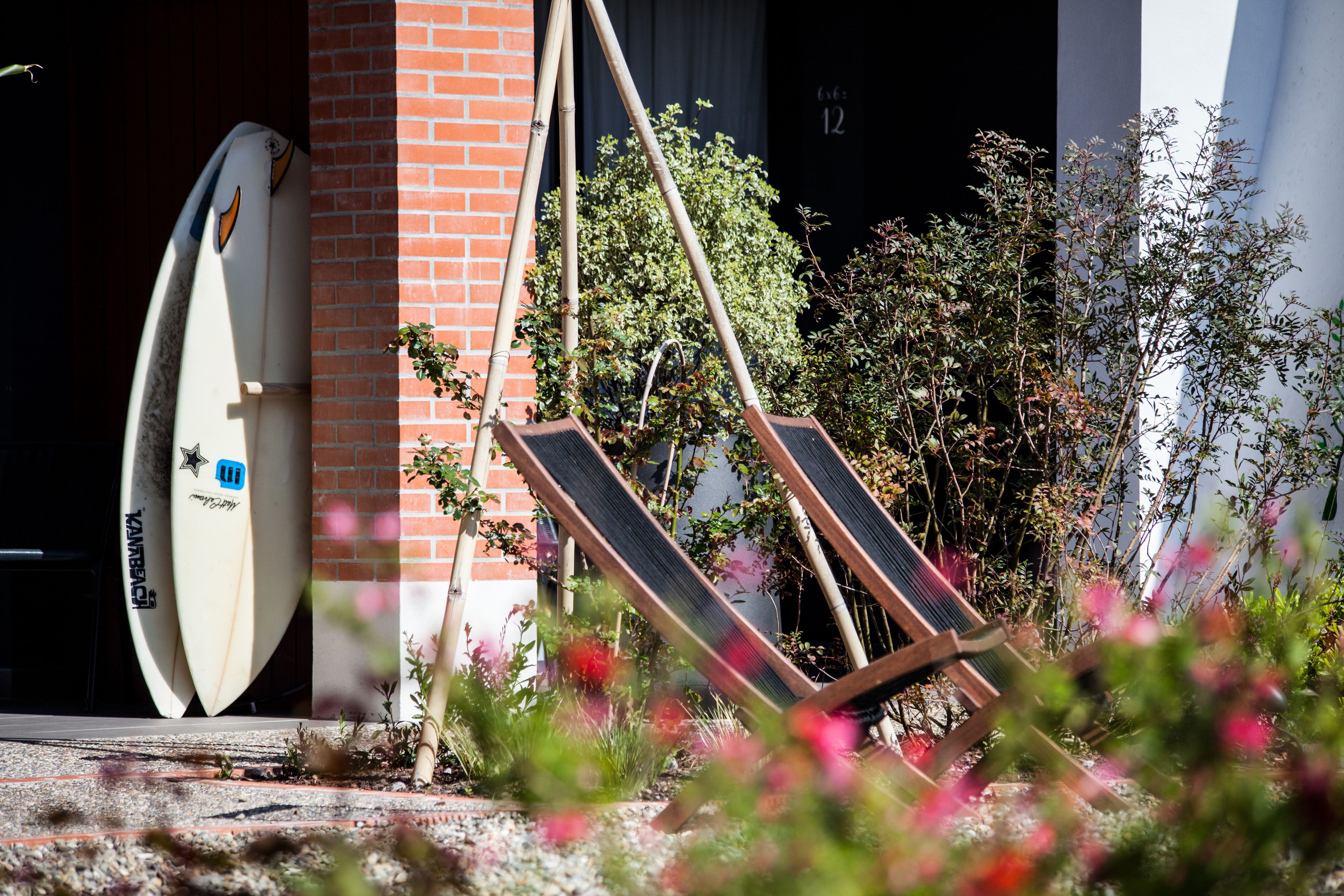 A surfboard leaning against a brick wall, a wooden chair, and a building entrance.
