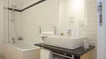 A modern bathroom with a white bathtub, a large sink, and a glass-enclosed shower area.