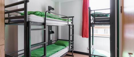 A dormitory room with bunk beds, a wooden wardrobe, a red curtain, and a window with a view.