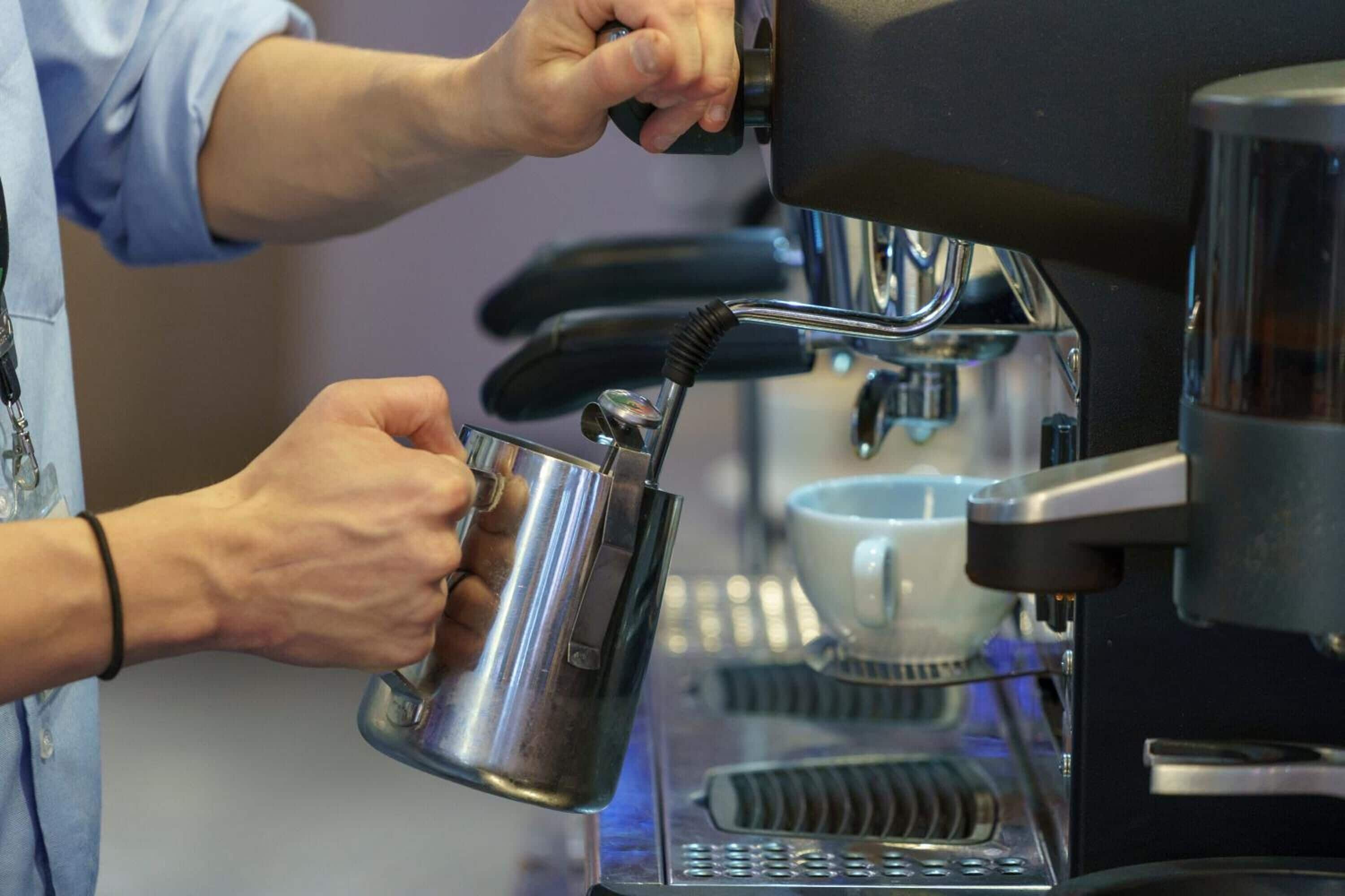 A person operating a coffee machine, holding a metal cup under the spout.