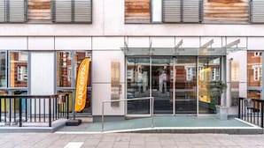 A modern building with a glass entrance, a yellow banner, and a sign that reads "CAFE OPEN". - YHA London Central - Hostel (London)