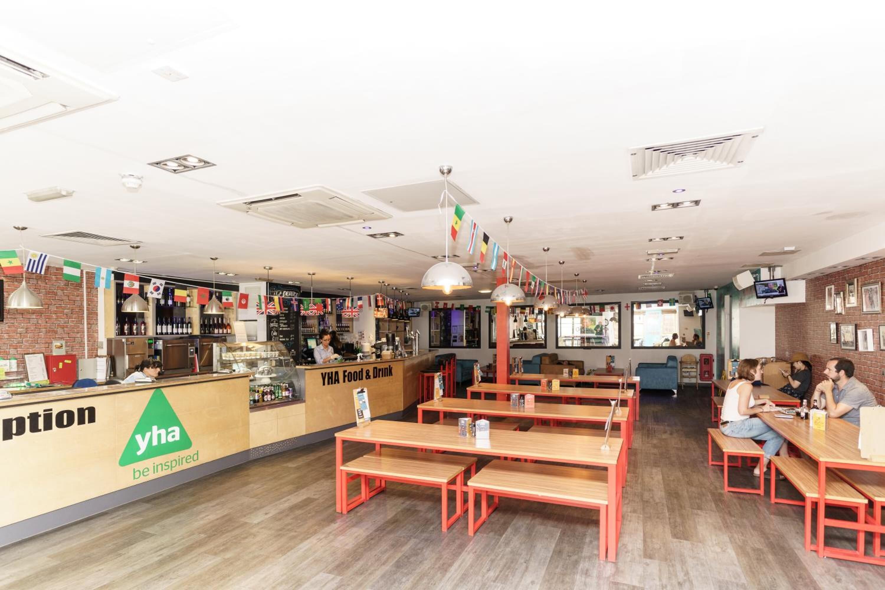 A restaurant with a counter, wooden tables, and benches.