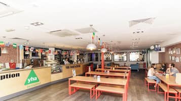 A restaurant with a counter, wooden tables, and benches.