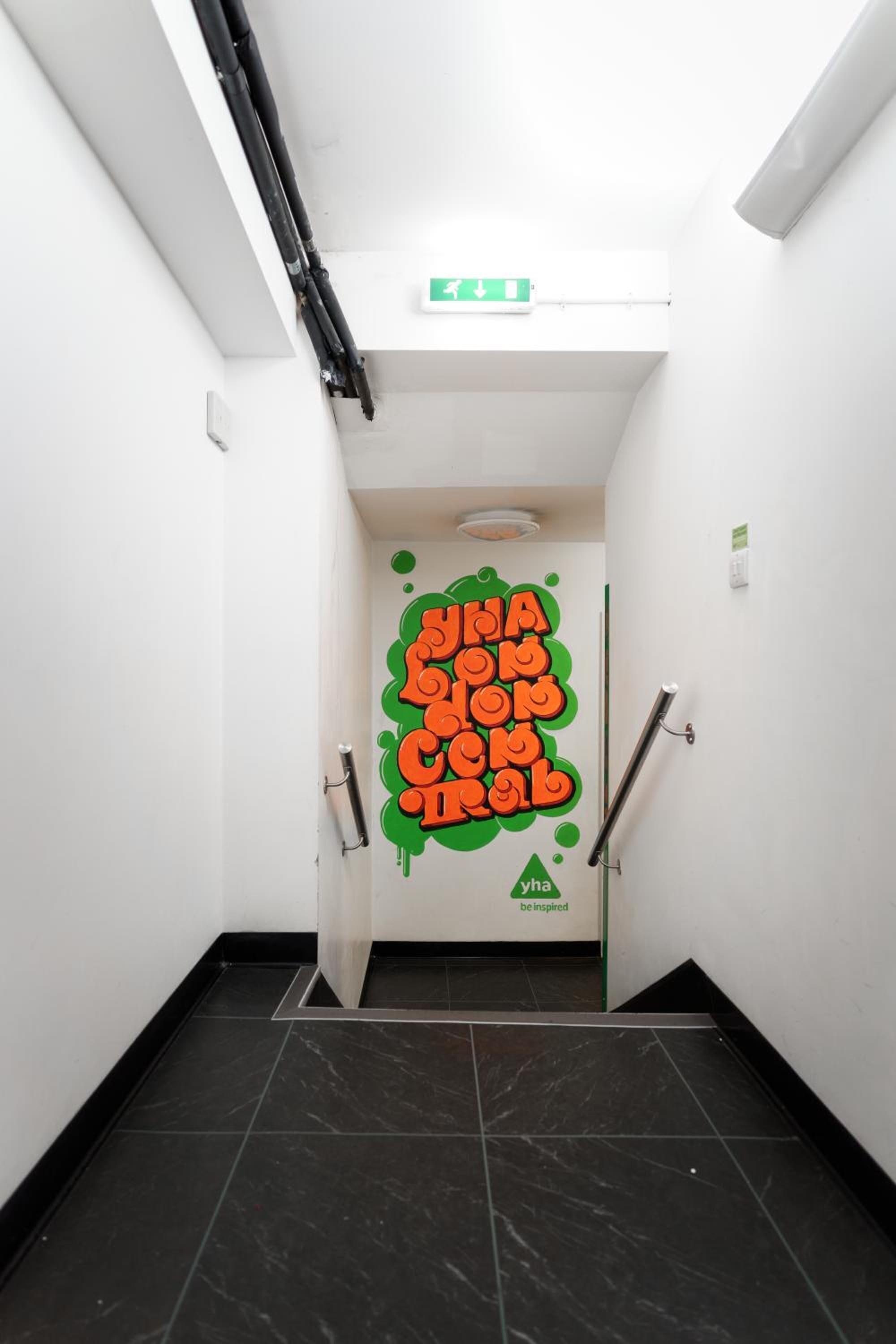 A narrow hallway with a black marble floor, white walls, and a green exit sign.