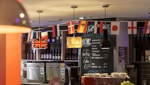 A coffee shop interior with a menu board, flags, and a variety of coffee and tea options. - YHA London Central - Hostel (London)