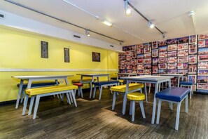 A brightly lit room with yellow walls, multiple tables and benches, and a wall adorned with numerous framed pictures. - YHA London Central - Hostel (London)