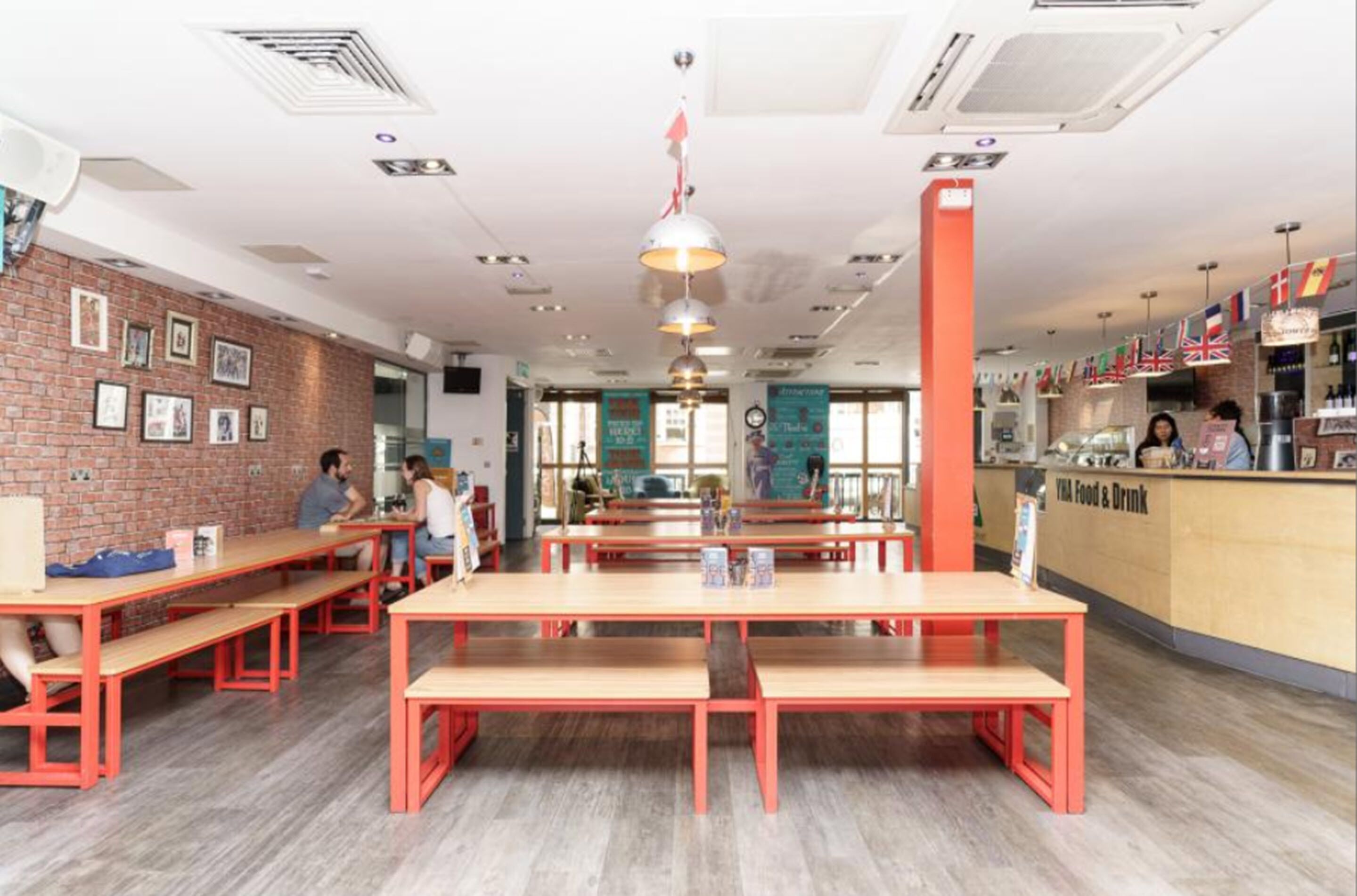 Un café moderno con bancos rojos, una pared de ladrillo con fotografías y un mostrador de comida y bebidas.
