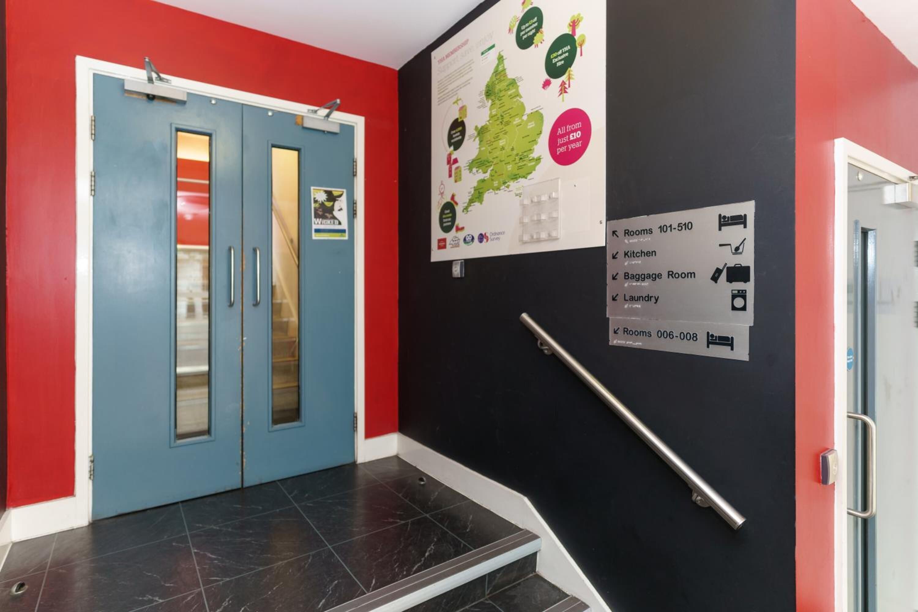 A hotel lobby with a blue door, a red wall, a map, and a sign listing room numbers and amenities.
