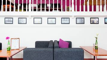 A modern lobby with a grey sofa, a wooden table with a clipboard and a pink flower, and a green bottle on a wooden table.