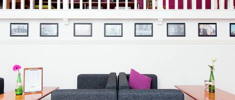 A modern lobby with a grey sofa, a wooden table with a clipboard and a pink flower, and a green bottle on a wooden table.