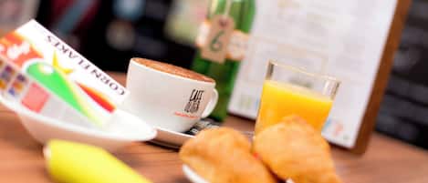 A breakfast setting with a croissant, a glass of orange juice, a coffee cup, and a menu on a clipboard.