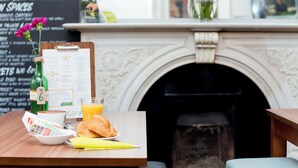 Una tavola imbandita per la colazione, con un menu, una bottiglia di succo, un cornetto e un vaso di fiori.