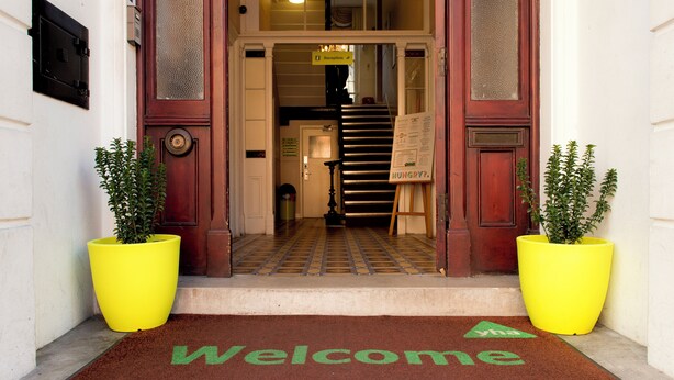 L'ingresso di un hotel con un tappetino 'Benvenuti', una reception e una scala che conduce ai piani superiori.