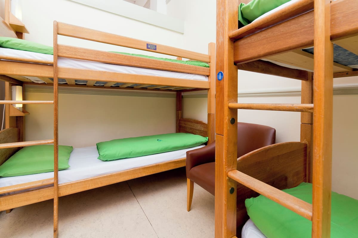 A bunk bed room with wooden frames, green pillows, and a brown chair.