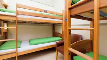 A bunk bed room with wooden frames, green pillows, and a brown chair.