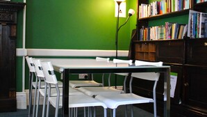 Una biblioteca con paredes verdes, una mesa blanca y sillas metálicas.