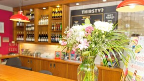 A bar area with a wooden counter, a vase of flowers, and shelves of bottles. - YHA Malham - Hostel (Skipton)