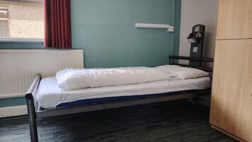 A single bed with white bedding in a room with teal walls, a radiator, and a wooden wardrobe.