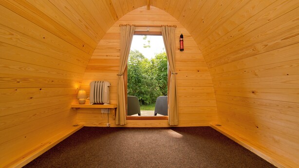 A cozy, wooden interior with a sloped ceiling, a small seating area with a chair and table, and a window with curtains. - YHA Malham - Hostel (Skipton)