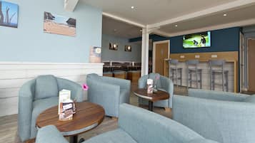 A modern lounge area with comfortable seating, a television screen, and artwork on the walls.
