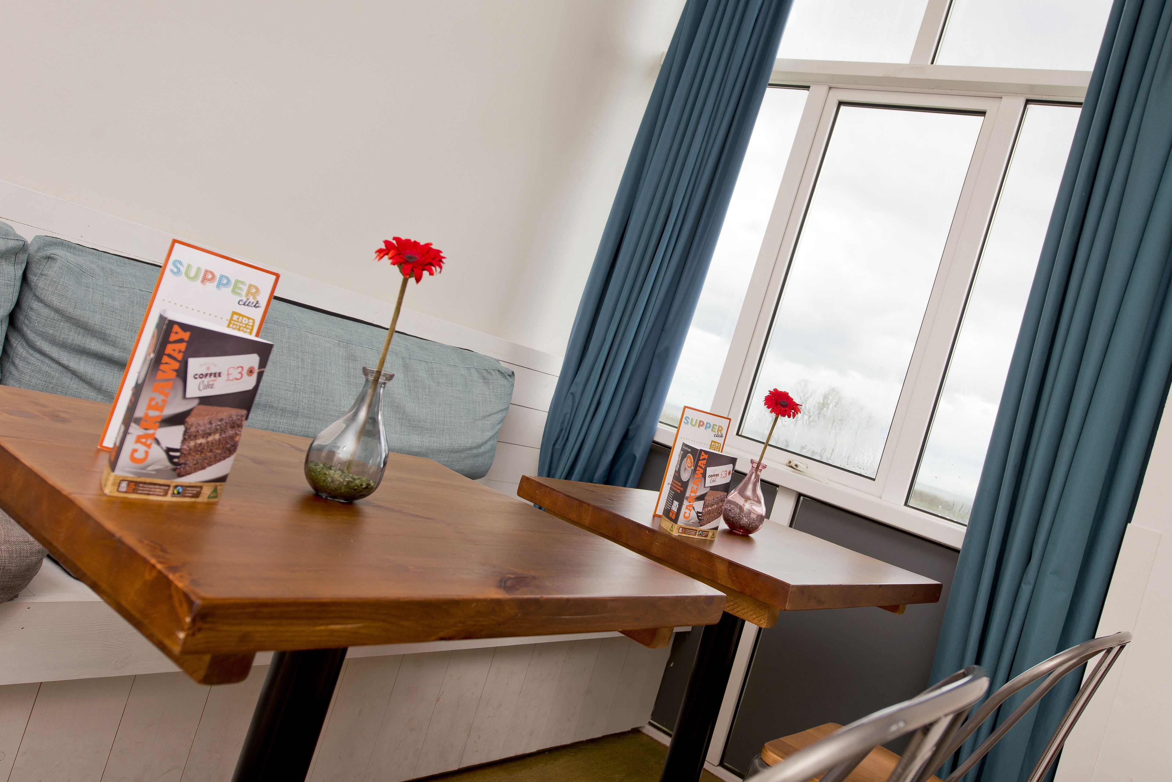 A wooden dining table with a vase of red flowers and a box of coffee.