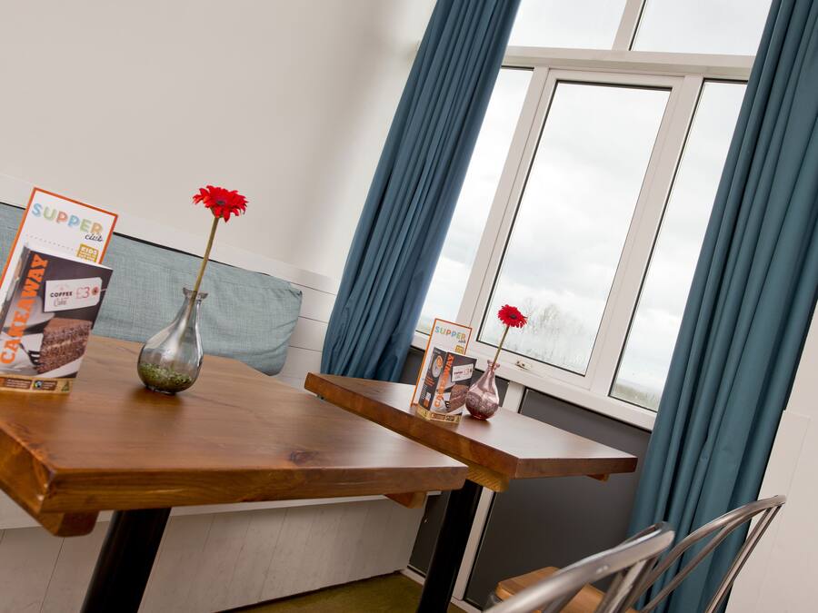 A wooden dining table with a vase of red flowers and a box of coffee.