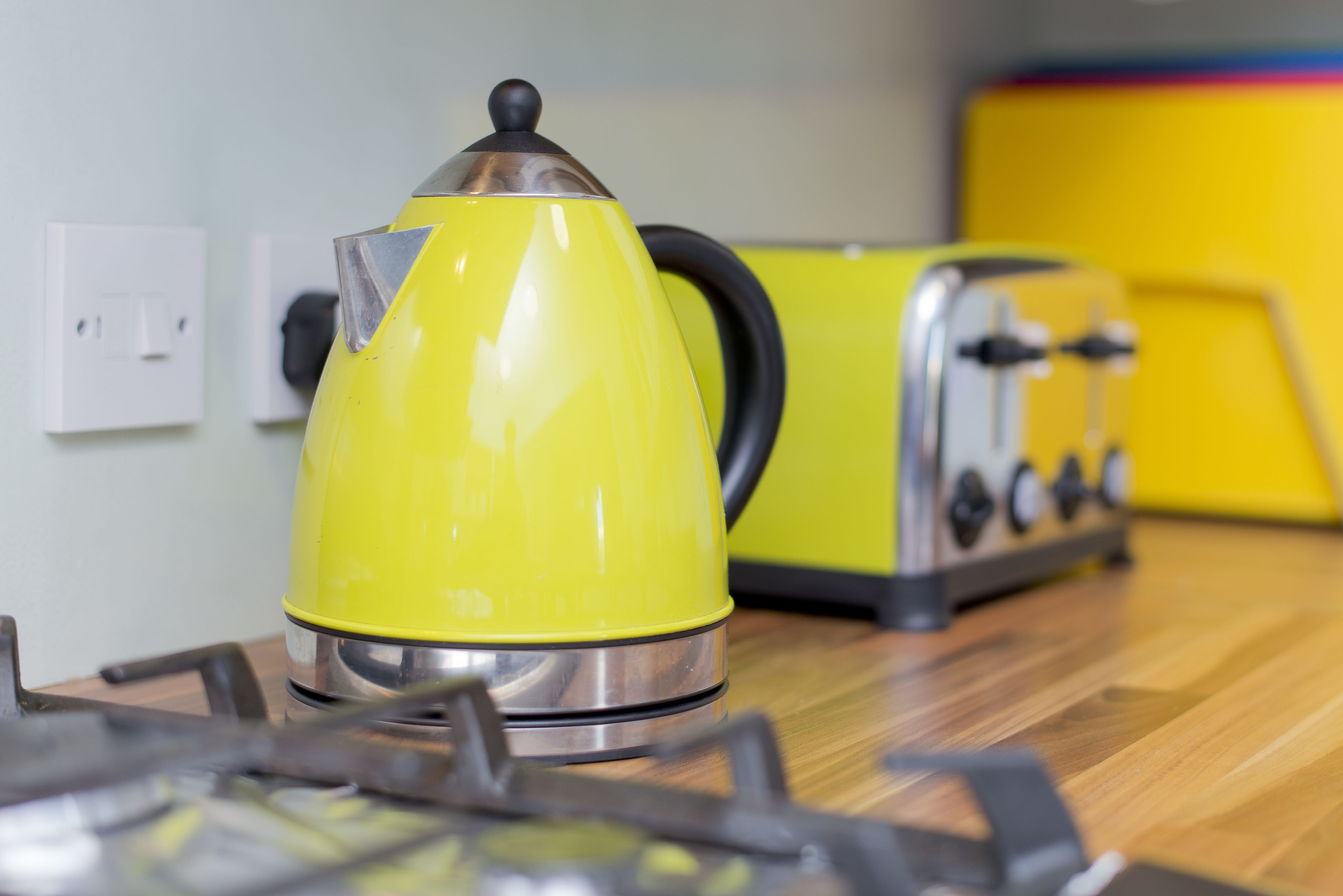 A yellow kettle on a stove, a yellow toaster, and a white electrical outlet on a wooden countertop.