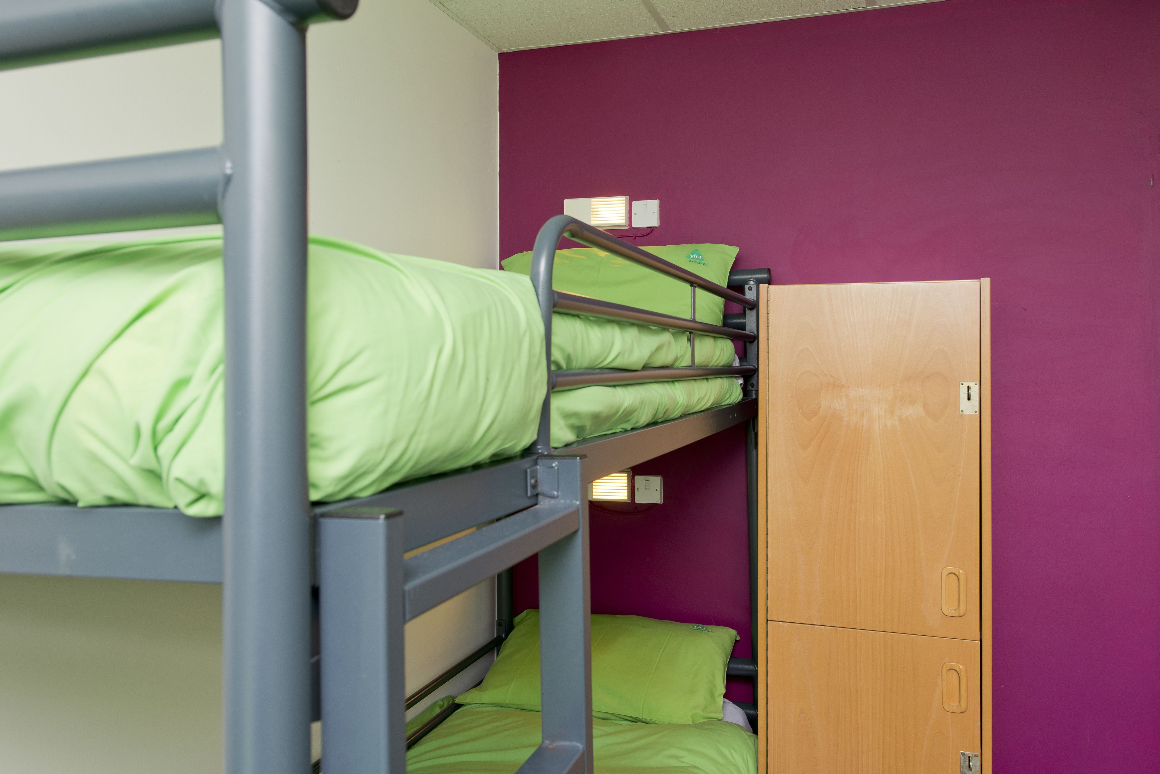 A bunk bed with green bedding, a wooden wardrobe, and a purple wall.