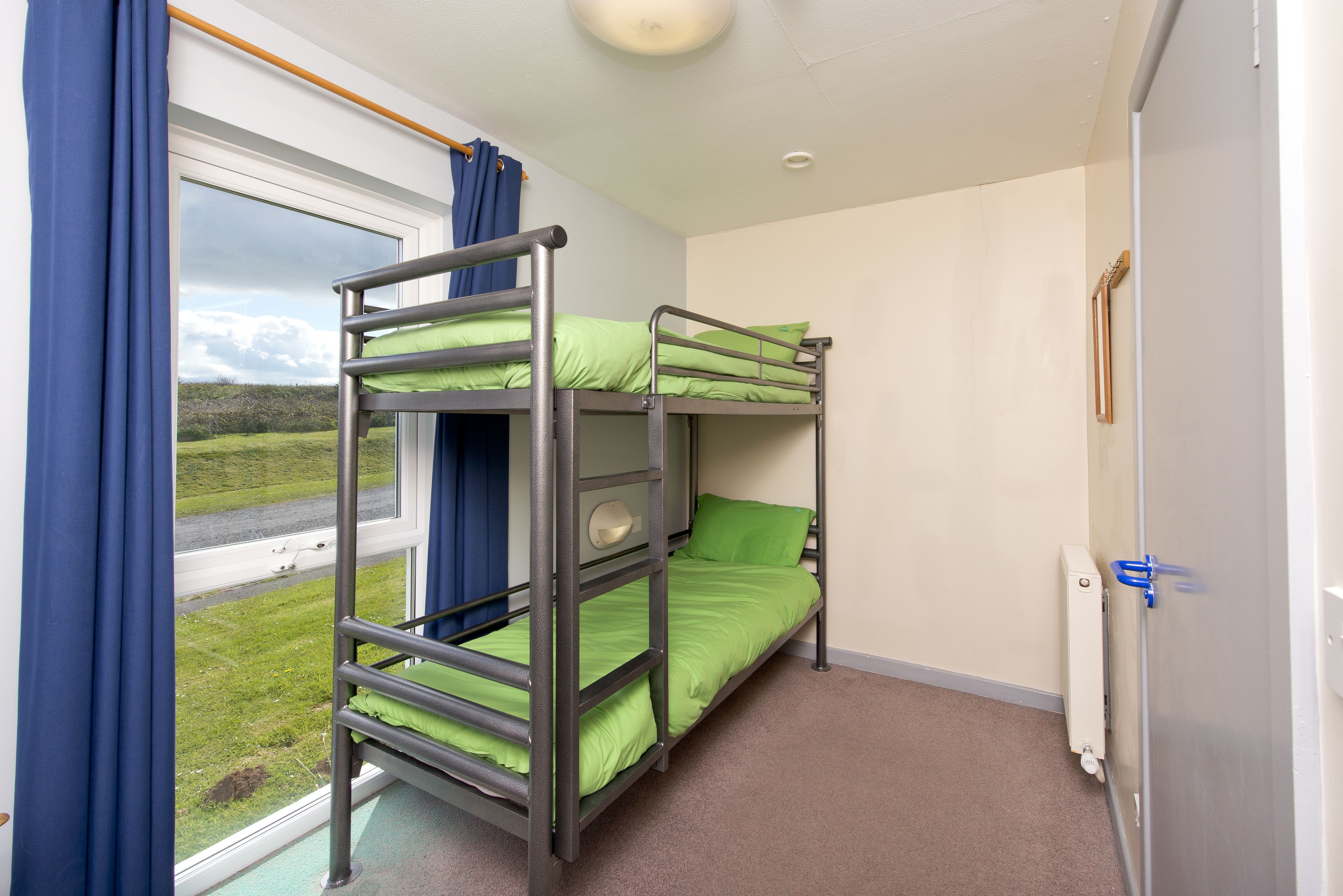 A bunk bed room with a window, curtains, and a radiator.