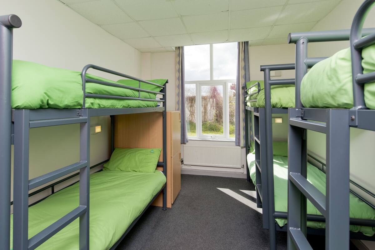 Une chambre de dortoir avec des lits superposés, une fenêtre et un radiateur.