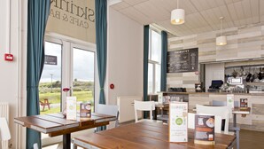 A café with wooden tables and white chairs, a menu board, and a view of the outdoors.